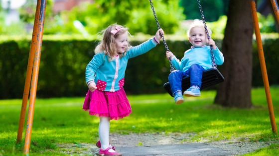 Little boy and girl on a playground. Child playing outdoors in summer. Kids play on school yard. Happy kid in kindergarten or preschool. Children having fun at daycare play ground. Toddler on a swing.